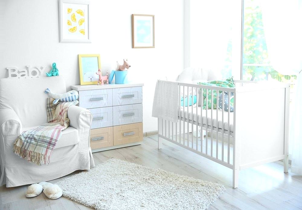 دکوراسیون اتاق خواب نوزاد که دارای دیوارهایی به رنگ خنثی یا سفید، تخت نوزاد سفید و مبل تکی می باشد